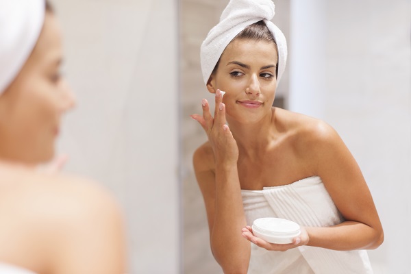 Idratazione profonda pelle Donna idrata la propria pelle davanti allo specchio.